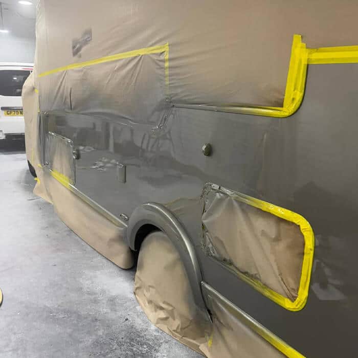 Specialist motorhome paintwork in progress. Meticulous masking of habitation windows and wheel arches during a professional grey metallic respray inside our Lostock Hall facility.