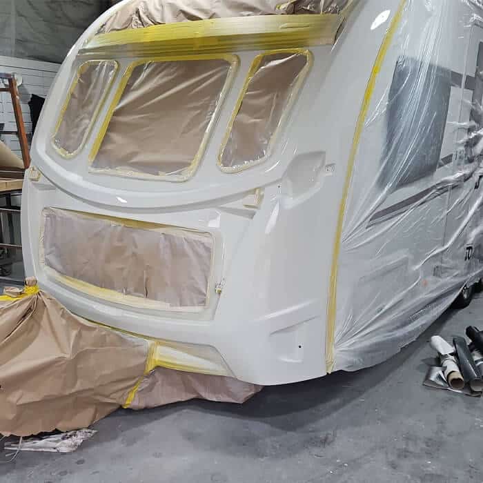 Front-end motorhome respray preparation in our Preston workshop. The front panel of a white coachbuilt motorhome is meticulously masked with yellow tape and protective paper, ensuring precision paintwork for the habitation area and window surrounds.