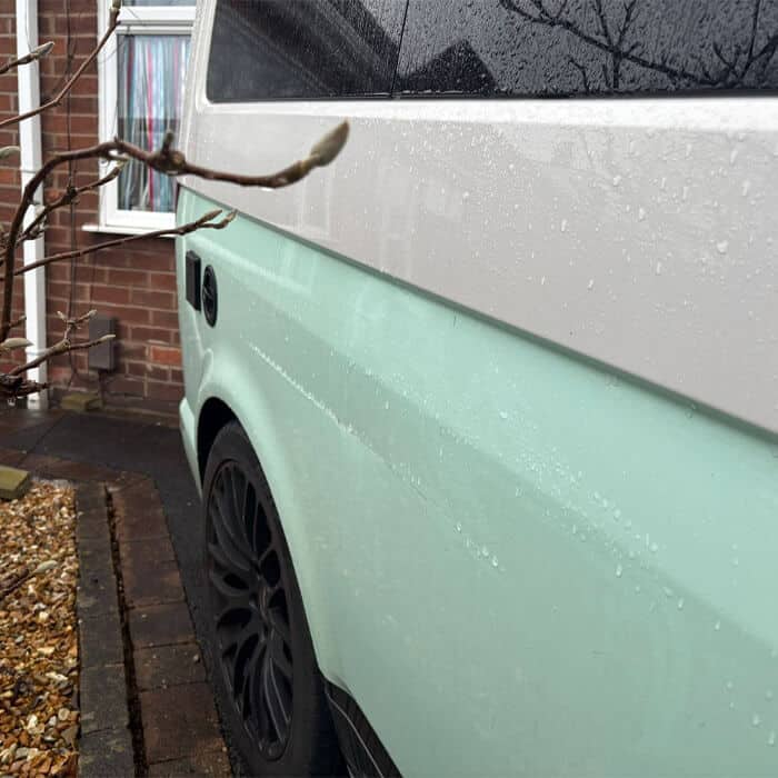 A close-up showing the professional gloss finish of a two-tone campervan respray in mint green and white. The high-quality specialist coachwork is evident in the rain-beaded surface, highlighting the durable, master-crafted finish delivered at our Lostock Hall facility.