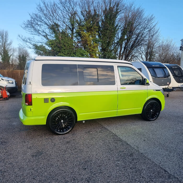 A completed bespoke motorhome respray on a Volkswagen Transporter, featuring a striking lime green and white two-tone finish with black alloy wheels. Professional specialist paintwork carried out at our Preston site, with other leisure vehicles visible in our secure yard.
